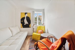 A room with a white sofa, a yellow armchair, a wicker chair, a small round table, and a painting on the wall. - Lovely holiday apartment in Rønne (Rønne)