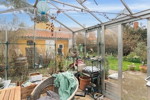 A conservatory with a glass roof, a wooden table, potted plants, and gardening tools. - Lovely holiday apartment in Rønne (Rønne)