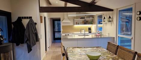 A modern kitchen with a central island, wooden beams on the ceiling, and a dining area with a patterned tablecloth.