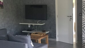 A modern living room with a grey sofa, a wooden coffee table, and a flat-screen TV mounted on the wall. - Maison de Vacance a 10 min du Circuit de spa Francorchamps et 5min de Spa (jalhay)