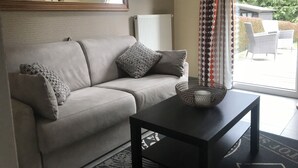 A living room with a sofa, a coffee table, a mirror, and a view of outdoor furniture through a window. - Maison de Vacance a 10 min du Circuit de spa Francorchamps et 5min de Spa (jalhay)