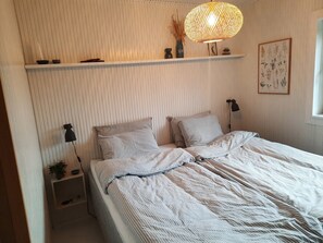 A neatly arranged bedroom with a bed, bedside tables, a hanging light fixture, and a wall-mounted shelf.