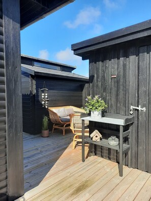 A wooden deck with a wicker chair and a small table with a potted plant.