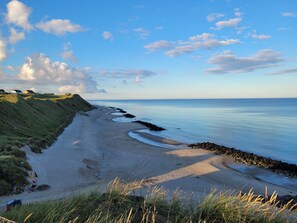 A coastal landscape with a sandy beach, grassy dunes, and a calm sea. - Cozy summer house in Lønstrup for 5 people. (lønstrup)