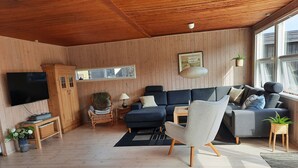 Ein modernes Wohnzimmer mit Holzboden, einem großen Flachbildfernseher, einem dunklen Sofa, einem hellen Sessel und einem Couchtisch aus Holz.