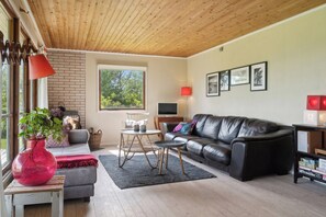 Een woonkamer met een zwarte leren bank, een klein rond tafeltje, een rode vaas en een raam met uitzicht op groen.