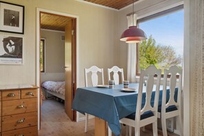 Een kamer met een eettafel, witte stoelen, een houten dressoir en een raam met uitzicht op bomen.