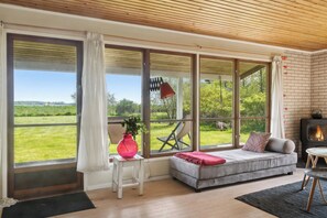 Een moderne woonkamer met grote ramen, een bank, een bijzettafeltje met een vaas en een open haard.