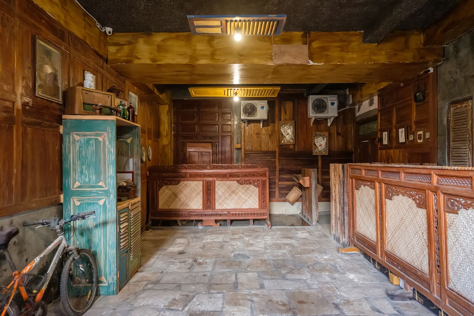 A rustic wooden interior with a stone floor, wooden furniture, and air conditioning units.