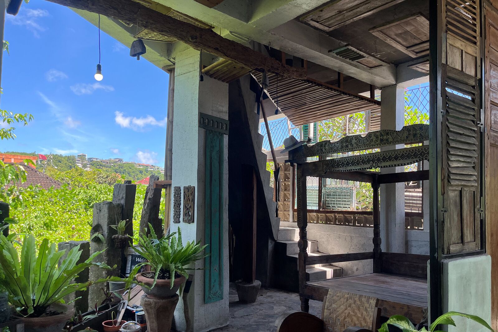 A covered outdoor area with a wooden bench, potted plants, and a view of a green landscape.