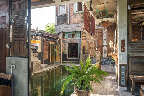 A traditional courtyard with a central water feature, wooden doors, and a hanging lantern. - TwoSpaces Living at Bunga Desa Jimbaran (Jimbaran)