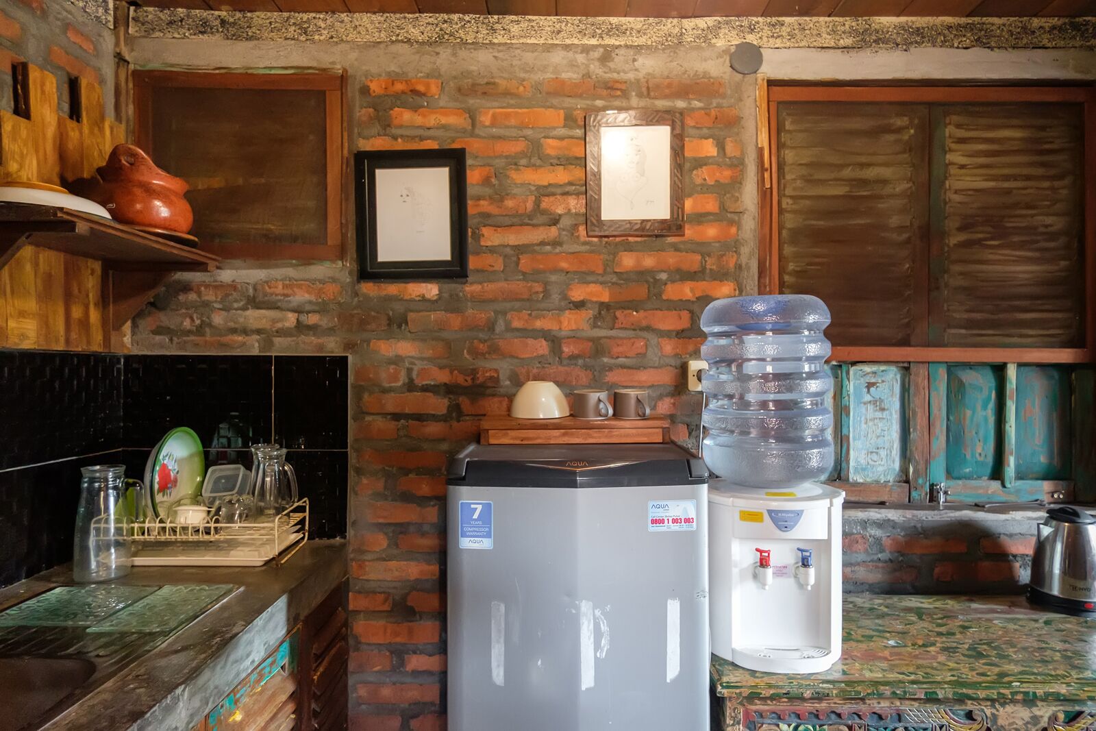 A kitchen with a brick wall, a refrigerator, a water dispenser, and a sink.