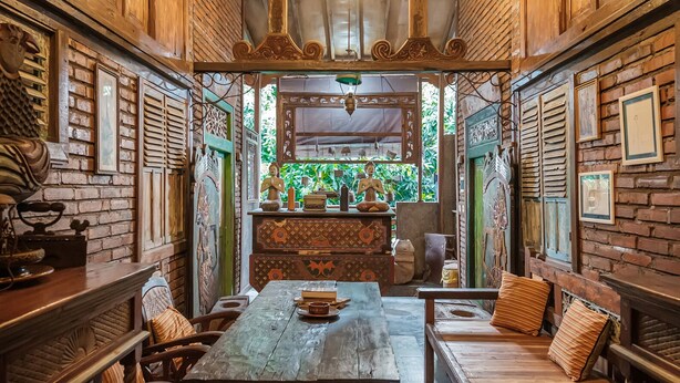 A rustic interior with a wooden table and benches, surrounded by brick walls and decorative elements. - TwoSpaces Living at Bunga Desa Jimbaran (Jimbaran)