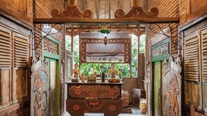 A traditional wooden room with intricate carvings, a central wooden cabinet, and a window with a view of greenery. - TwoSpaces Living at Bunga Desa Jimbaran (Jimbaran)