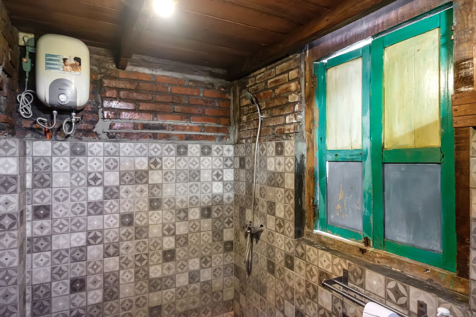 Un baño con baldosas estampadas, ducha, ventana con marco verde y calentador de agua.