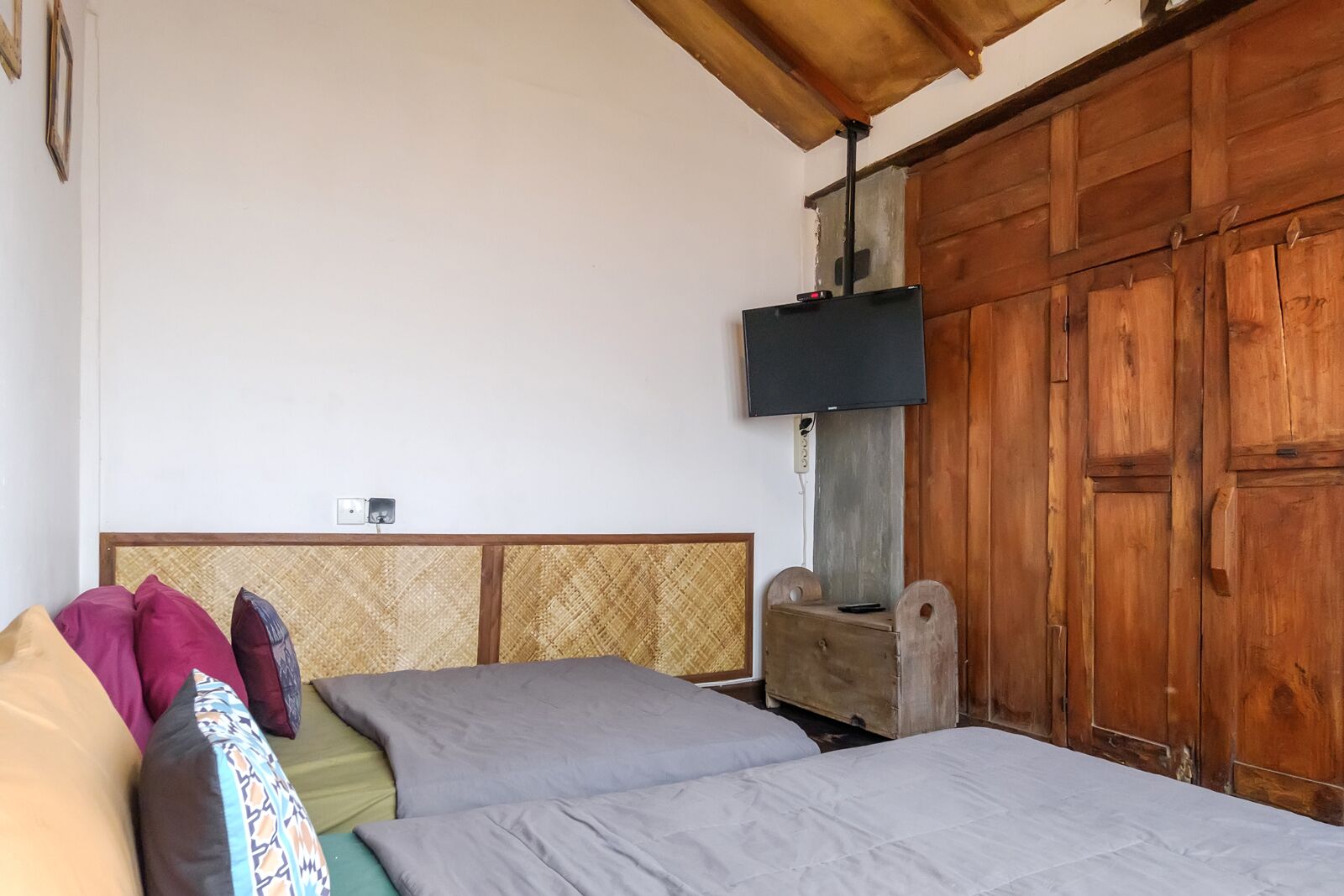 Un dormitorio con cama, almohadas, un armario de madera y televisión.