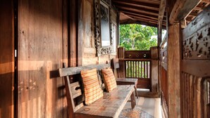 A wooden porch with a bench and a table, a decorative gate, and a view of greenery outside. - TwoSpaces Living at Bunga Desa Jimbaran (Jimbaran)
