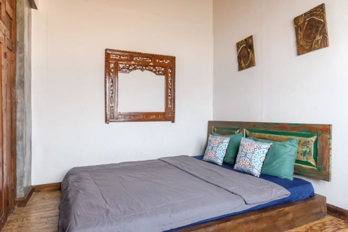 A bedroom with a wooden headboard, a bed with grey bedding, and two decorative pillows.