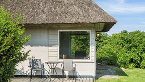 Een huis met rieten dak, een houten terras, twee stoelen en een tafel.