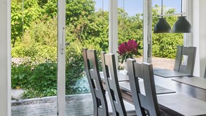 Een eetgedeelte met uitzicht op een tuin, een tafel met stoelen en hanglampen.