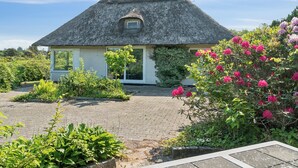 Een huis met rieten dak, een verharde oprit en een tuin met bloeiende planten.