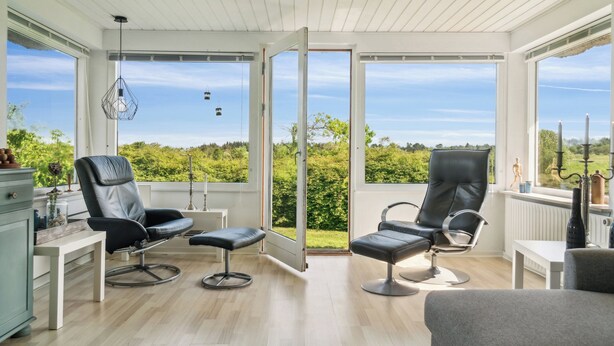 Een ruim balkon met twee leren stoelen en een bankje, met uitzicht op een weelderig groen landschap.