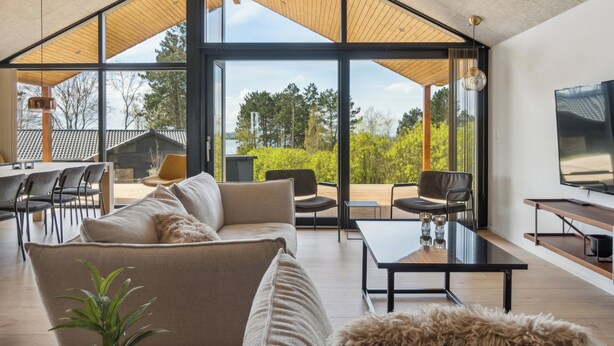 A modern living room with a large window, a sofa, a coffee table, and a TV. - Impressive holiday cottage, by the Helsnæs Bay! (Millinge)