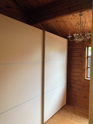 Una habitación con paredes y suelo de madera, una puerta corredera y una araña.