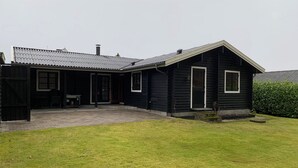 Une maison en bois peinte en noir, avec une terrasse carrelée et une cour gazonnée.