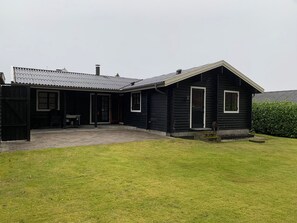 A black wooden house with a tiled patio and a grassy yard.