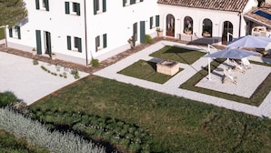 Un edificio grande y blanco con techo de tejas, numerosas ventanas y un patio con mesas al aire libre.