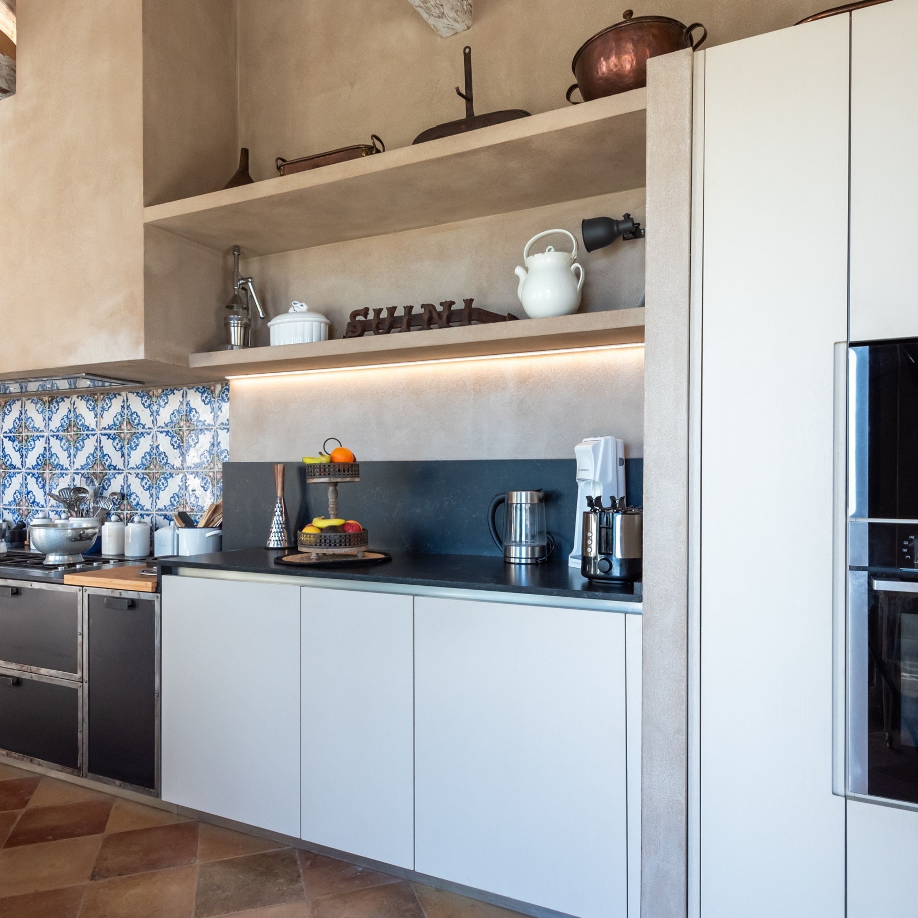 Une cuisine moderne avec des meubles blancs, un plan de travail noir et divers appareils de cuisine.