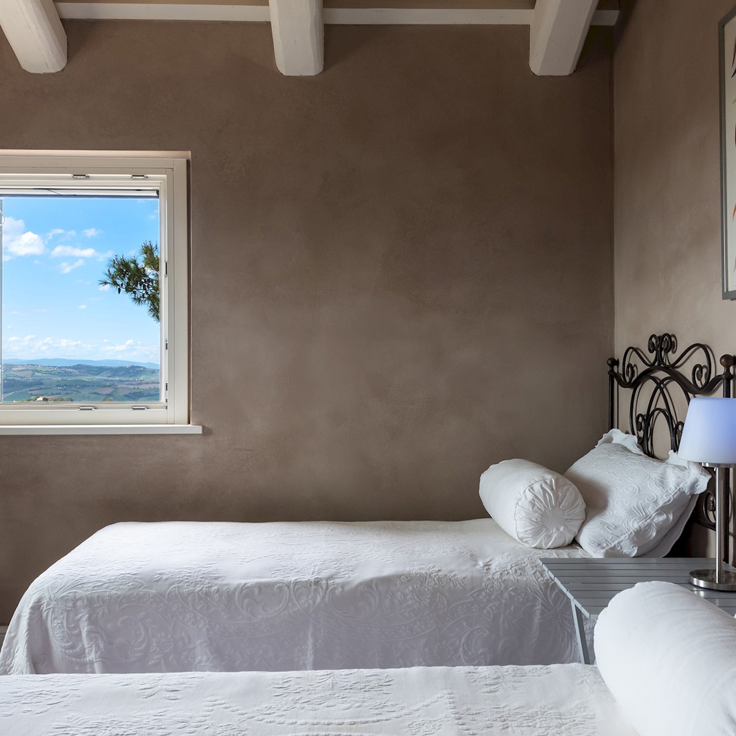 Ein Schlafzimmer mit zwei Betten, einem Fenster mit Blick auf die Landschaft und einem Nachttisch mit Lampe.