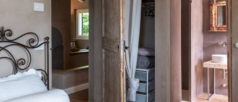 Un dormitorio con cama, armario y baño visible a través de una puerta abierta.