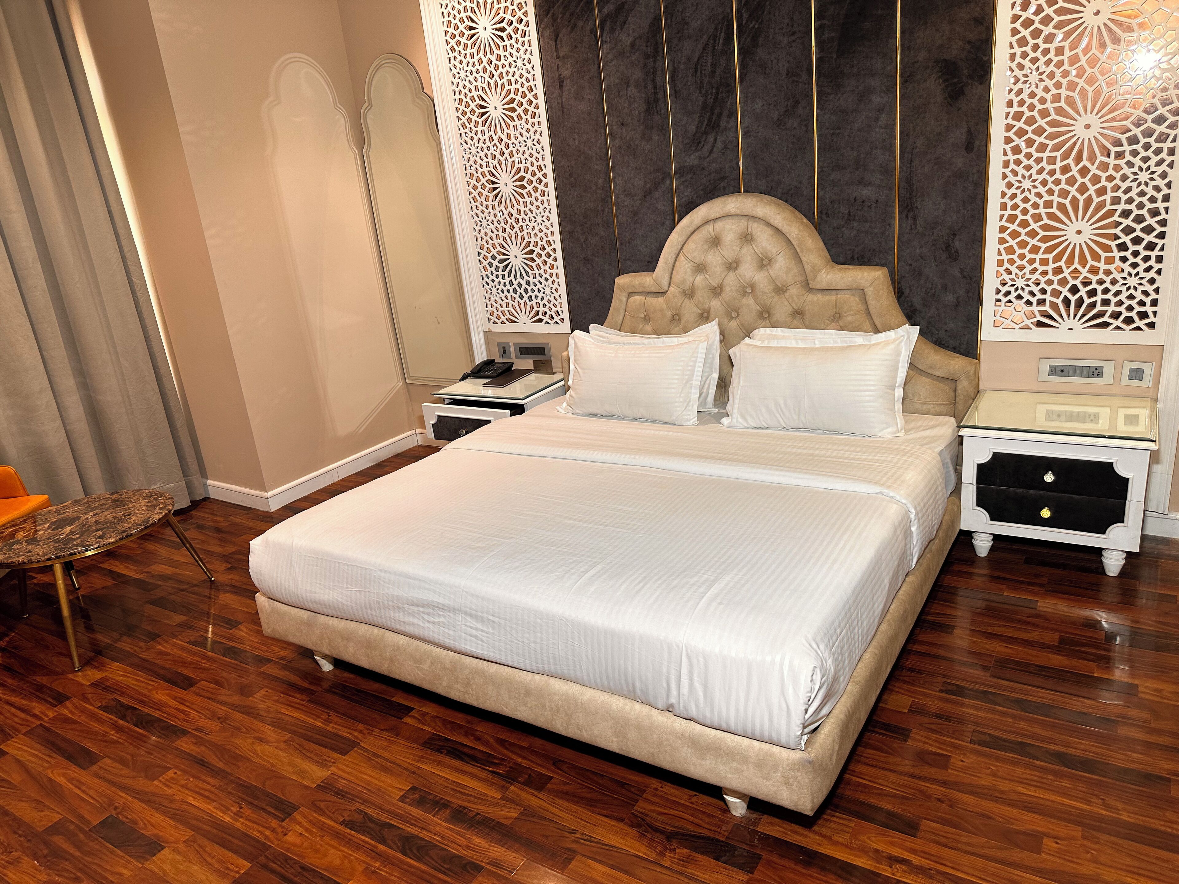 A large bed with a tufted headboard, two bedside tables, and a nightstand with a phone and a lamp.