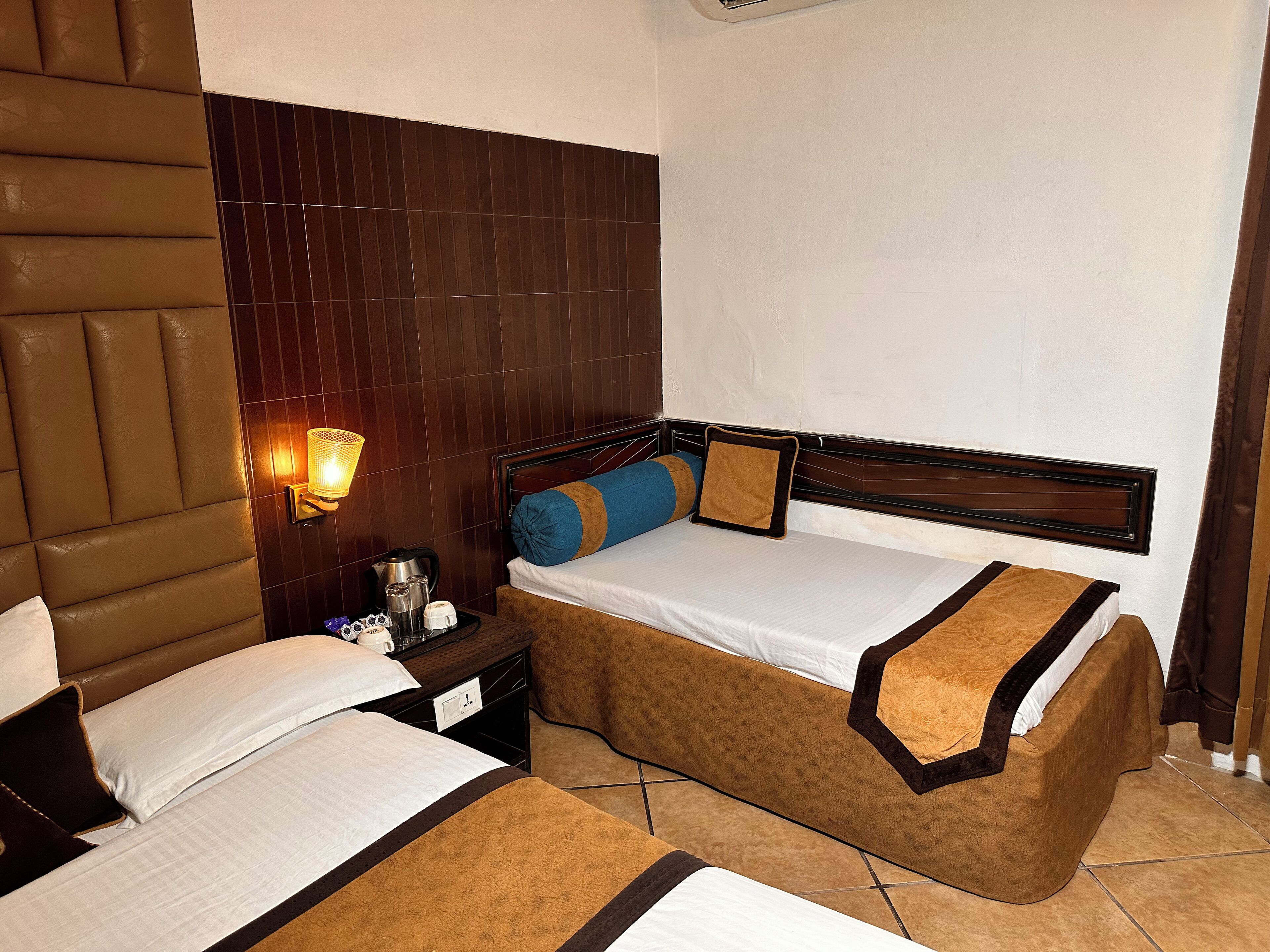 A hotel room with two beds, a nightstand with a lamp, and a wooden headboard.
