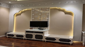 A modern entertainment unit with a flat-screen TV, decorative paneling, and built-in speakers. - Devrath By Big Bite Resort (Meerut)