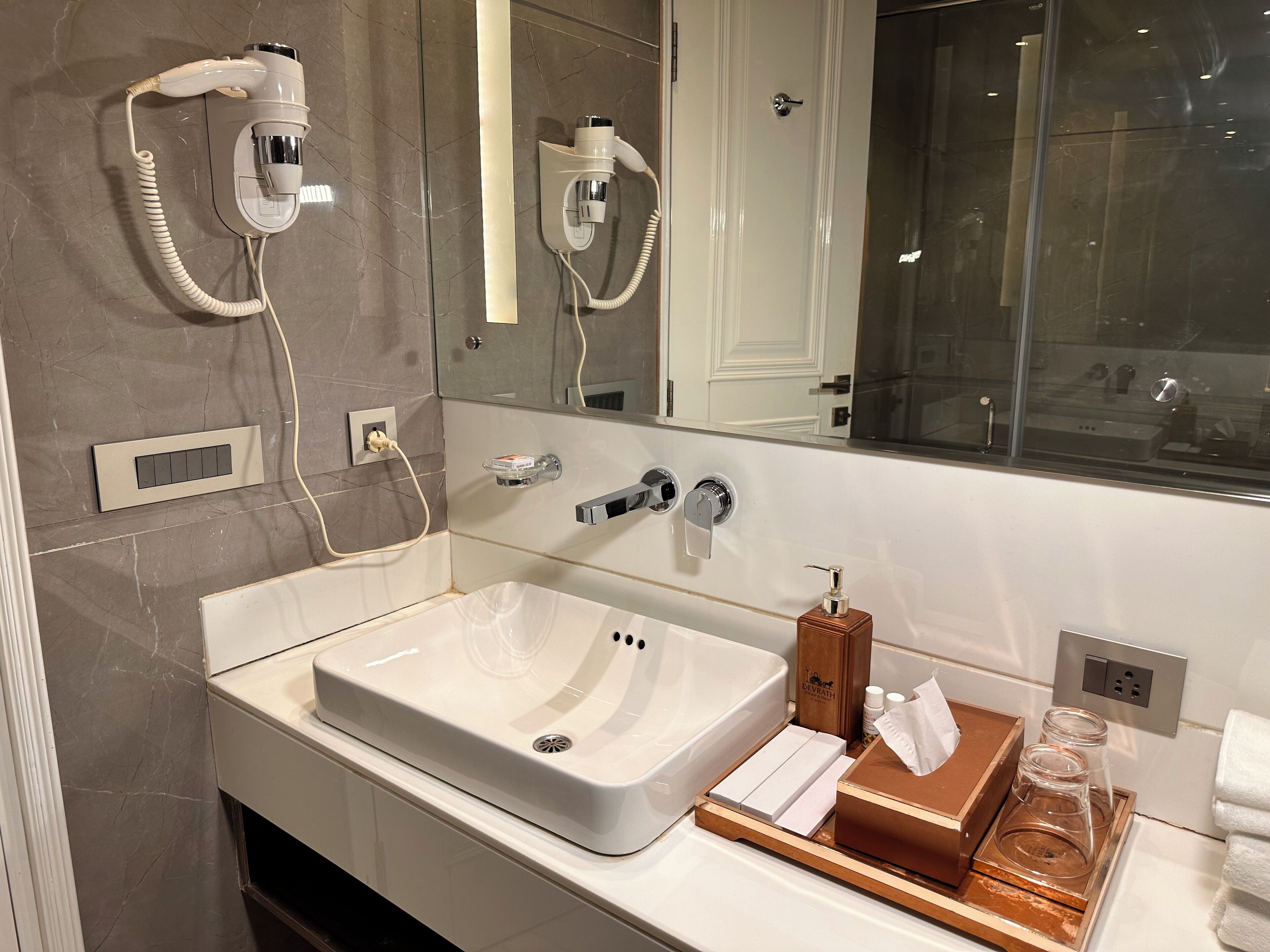 A modern bathroom with a large sink, a hairdryer, a mirror, and a window.