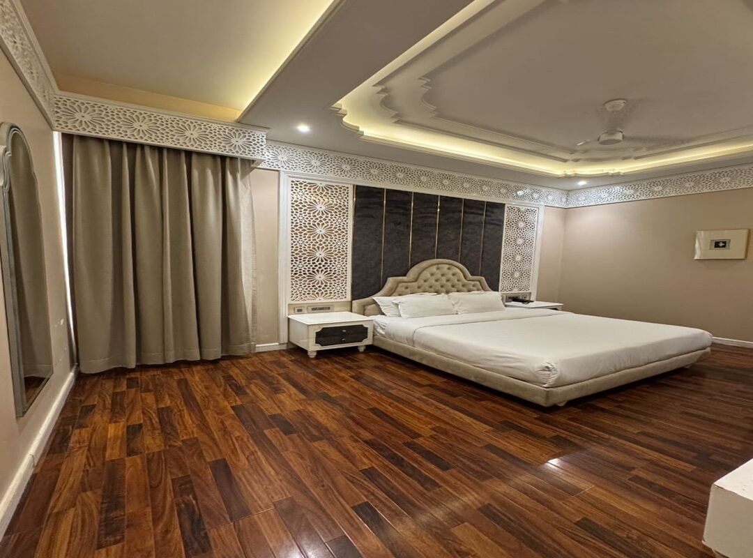 Een slaapkamer met een groot bed, houten vloeren, een decoratief plafond en een nachtkastje.