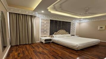 Een slaapkamer met een groot bed, houten vloeren, een decoratief plafond en een nachtkastje.
