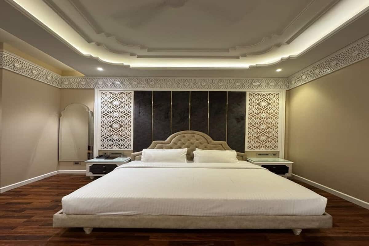 Uma cama grande com cabeceira estofada, duas mesas de cabeceira e painéis decorativos na parede.