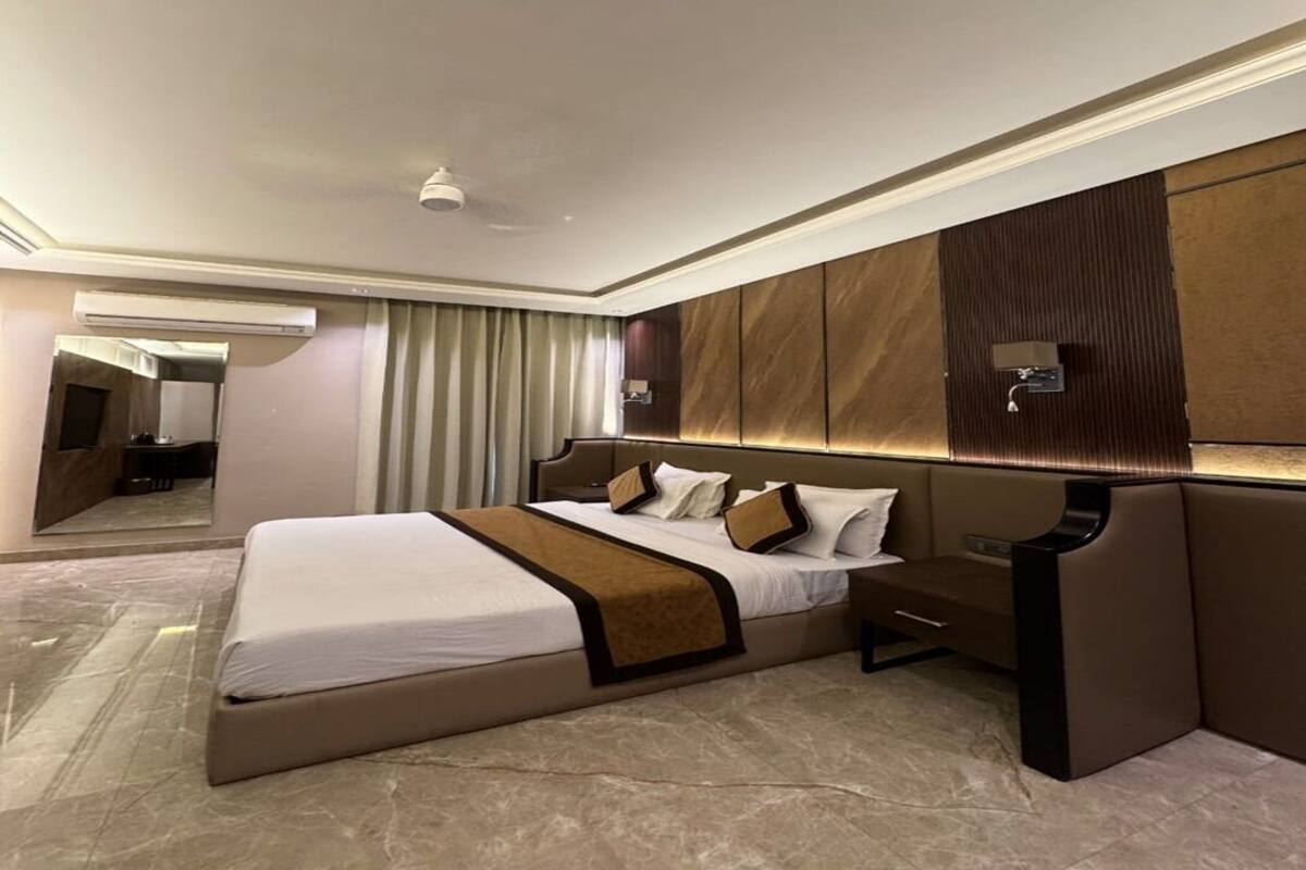 Quarto de hotel moderno com uma cama grande, mesa de cabeceira, espelho e televisão fixada na parede.