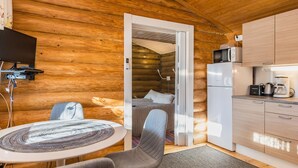 Ein gemütliches Blockhaus mit Holzinnenausbau, einer kleinen Küchenzeile, einem Bett und einem Fernseher.