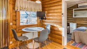 Ein gemütliches Blockhaus-Interieur mit Holzvertäfelung, einem runden Tisch mit zwei Stühlen, einem Fernseher und einem Bett mit gesteppter Bettdecke.