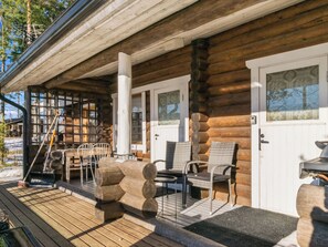 Une cabane en rondins avec un porche, des sièges d’extérieur et une porte dotée d’une fenêtre.
