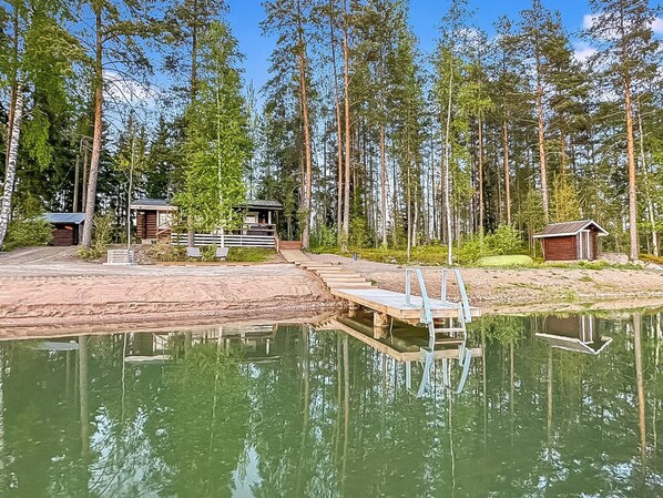 A lakeside cabin with a dock extending into the water, surrounded by tall trees.
