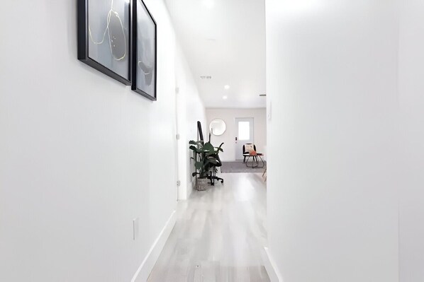 A modern, well-lit hallway with a minimalist design, featuring a desk and chairs in the distance.
