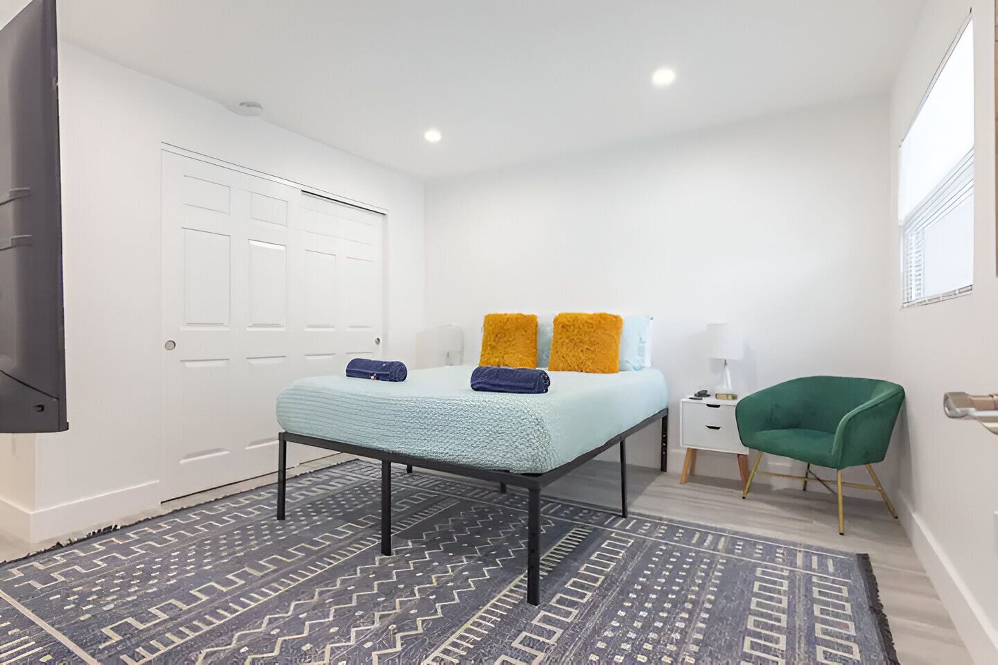 A bedroom with a bed, a green chair, a nightstand, and a white door.