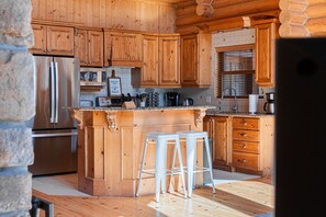 A kitchen with wooden cabinets, a stainless steel refrigerator, a coffee maker, and a bar stool.