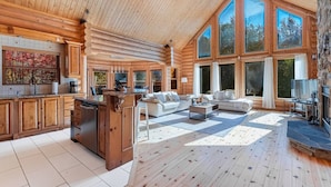 Un intérieur spacieux de chalet en bois, comprenant une cuisine, un espace de vie et de grandes fenêtres.